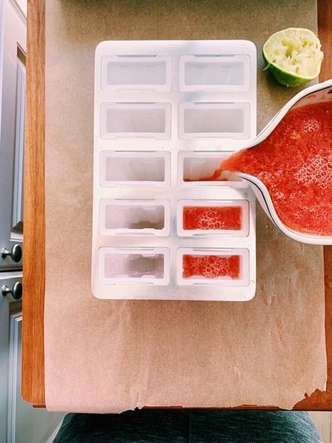 Blended watermelon, lime juice and mint syrup being poured into a popsicle mold