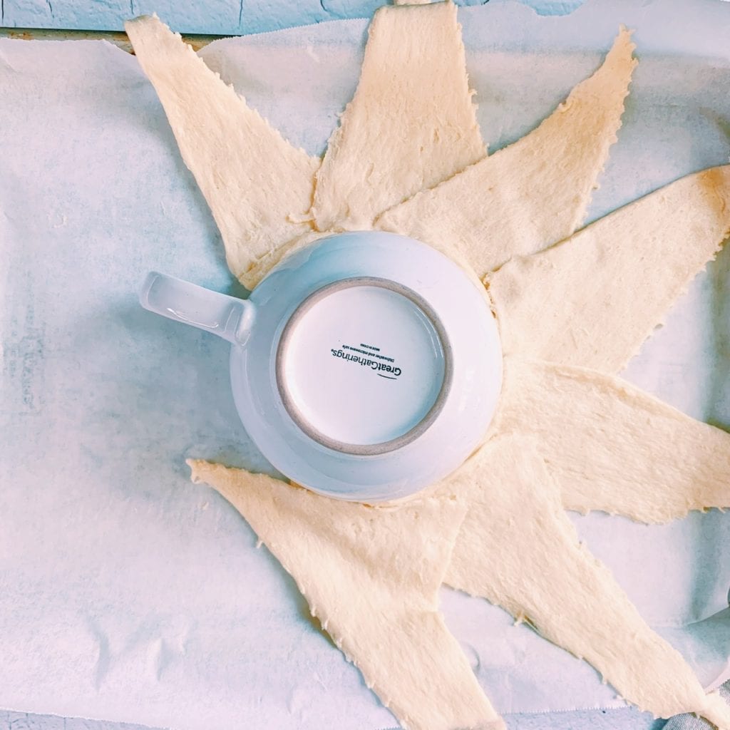 Crescent roll triangles arranged around a bowl on a baking sheet. 