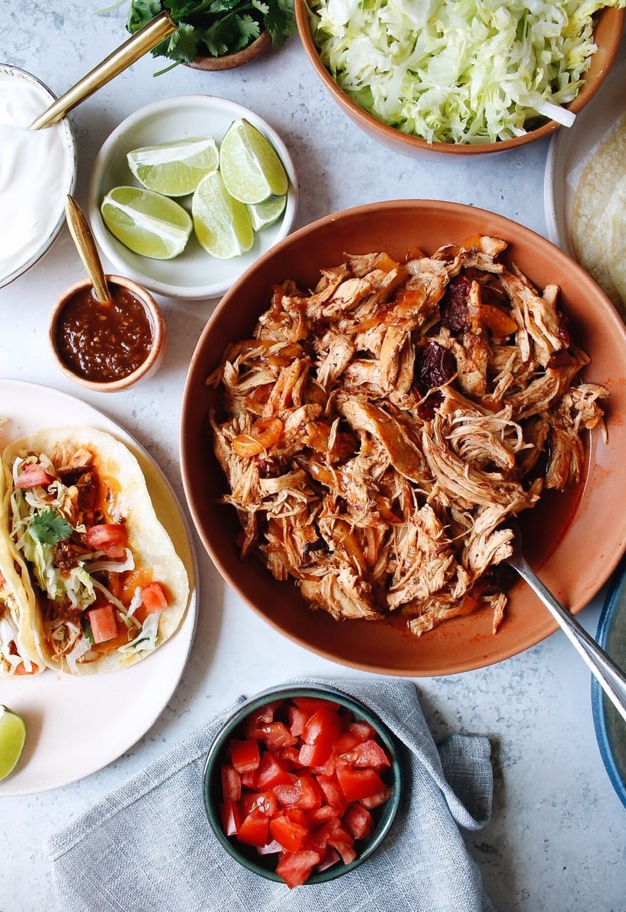 slow cooker chipotle chicken in a bowl next to a plate of tacos