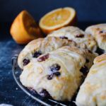 side view of cranberry orange sourdough scones on a circular cooling rack with oranges in the background