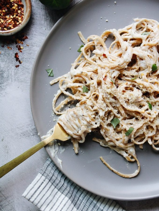 Fettuccini alfredo on a gray plate topped with basil and pepper flakes
