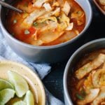 two bowls of chicken tortilla soup with a bowl of limes