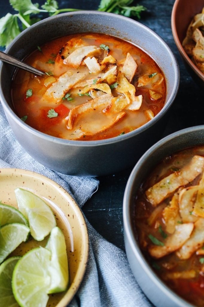 two bowls of chicken tortilla soup with a bowl of limes 