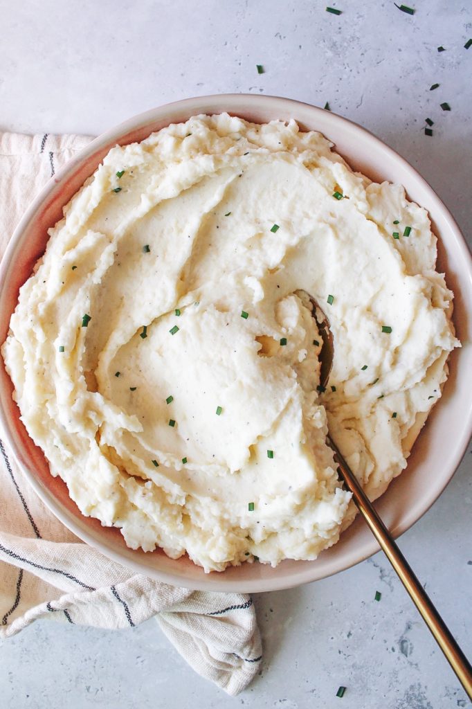 cream cheese and chive mashed potatoes in a large bowl with a gold serving spoon