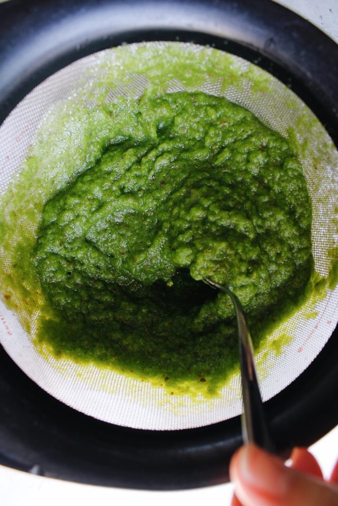 kale apple celery juice pulp being put through a strainer