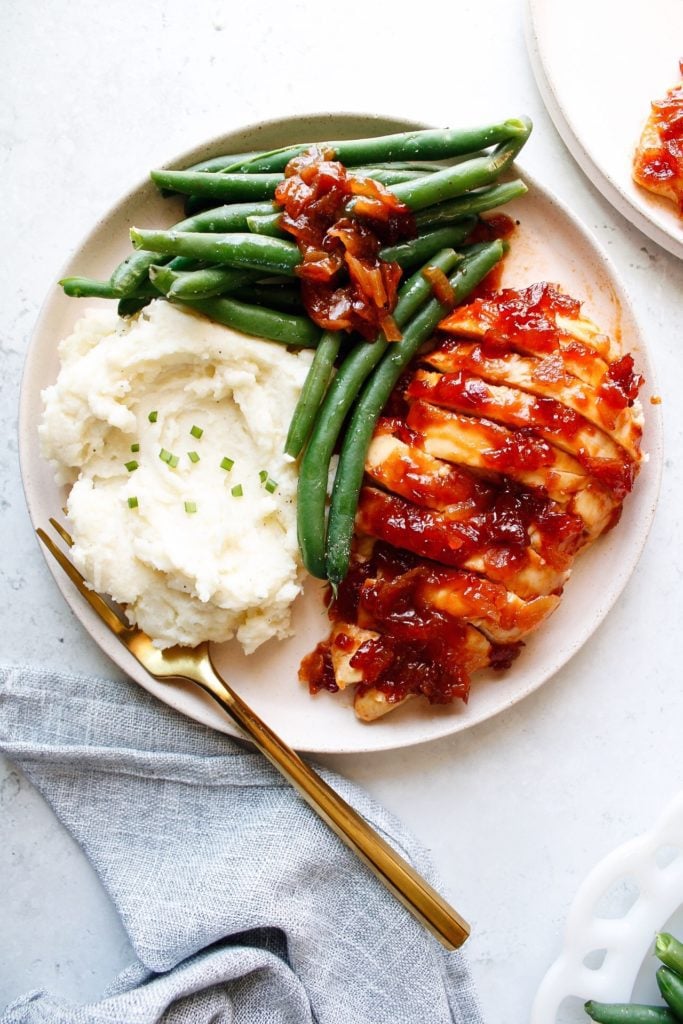 baked saucy chicken on a plate with mashed potatoes and green beans