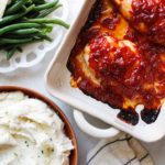 baked saucy chicken on a table with green beans and mashed potatoes