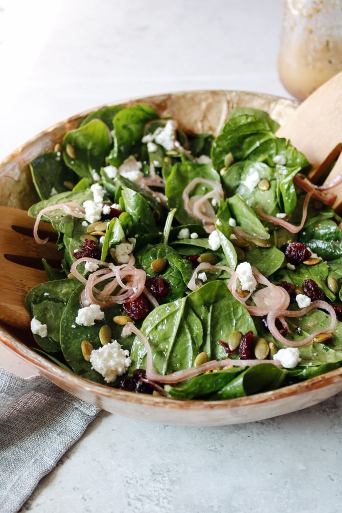 spinach goat cheese salad with salad tossers in the bowl