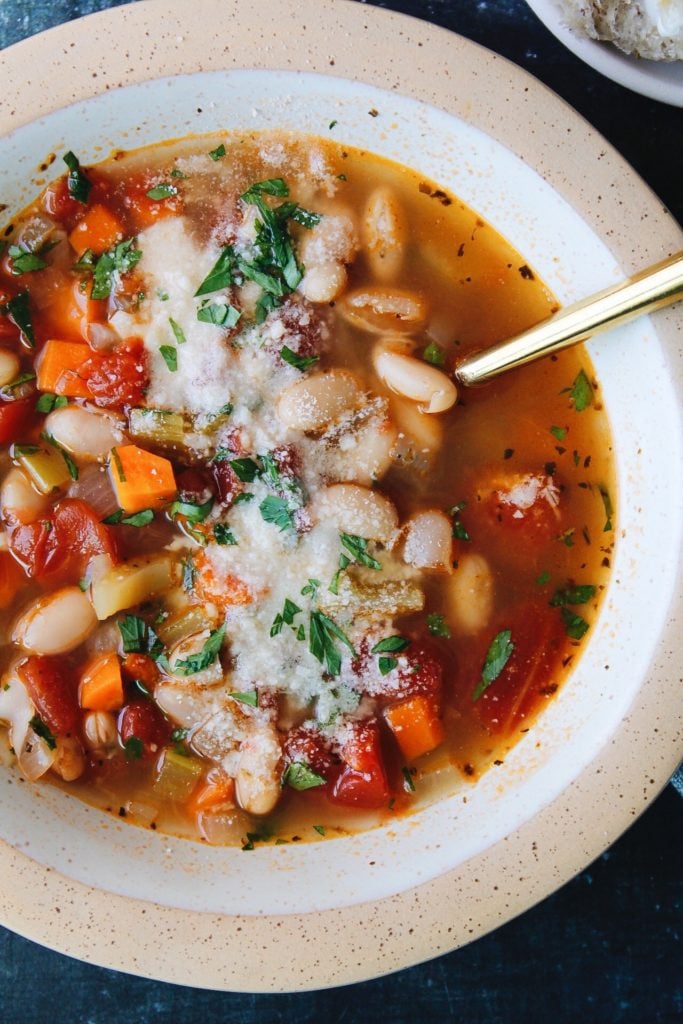 vegetable bean soup in an beige bowl topped with parmesan cheese