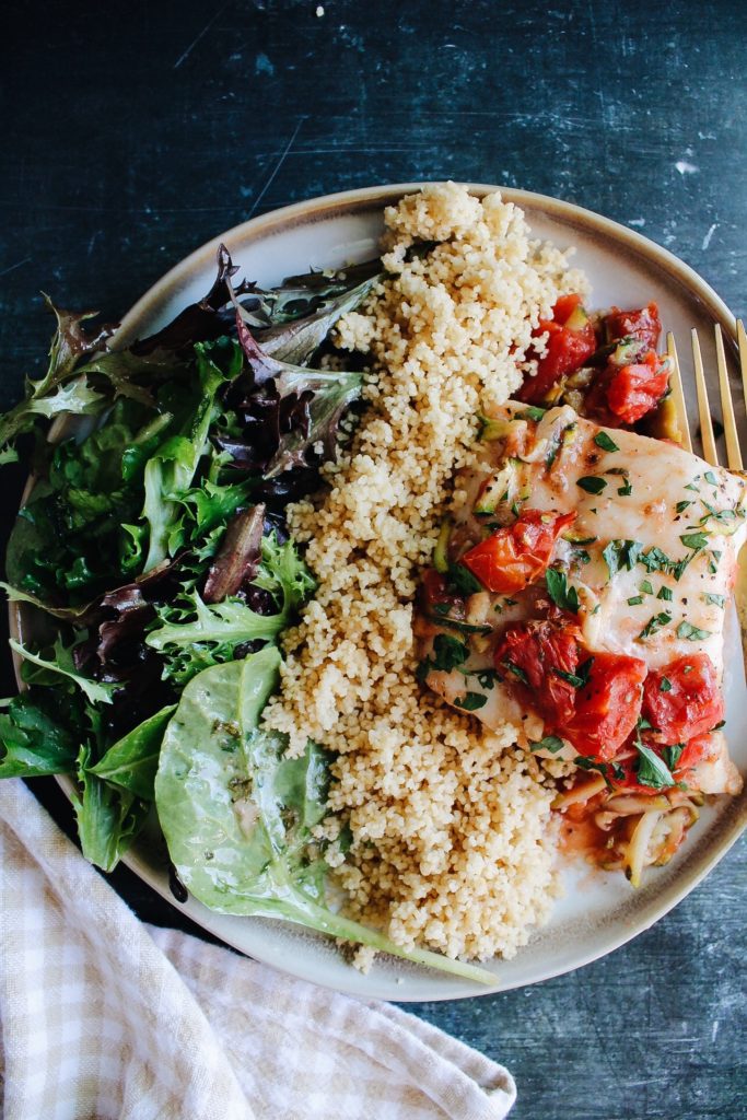italian baked fish in tomatoes plated with couscous and a salad