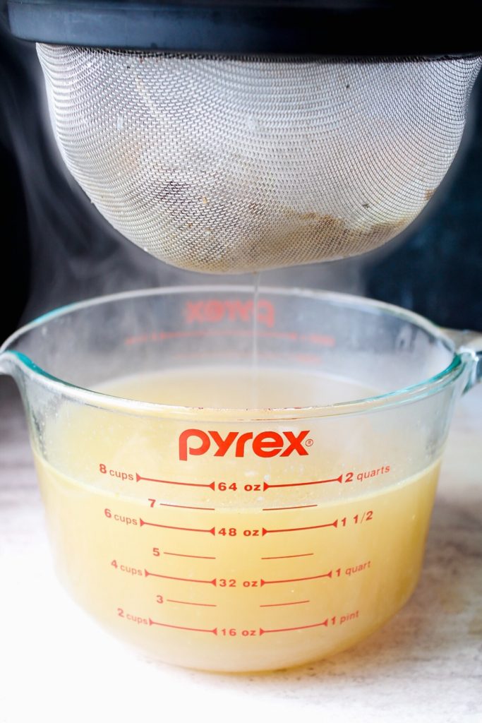 homemade chicken stock being strained into a large measuring cup
