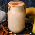 peanut butter banana date oat milk smoothie in a clear glass jar topped with extra peanut butter