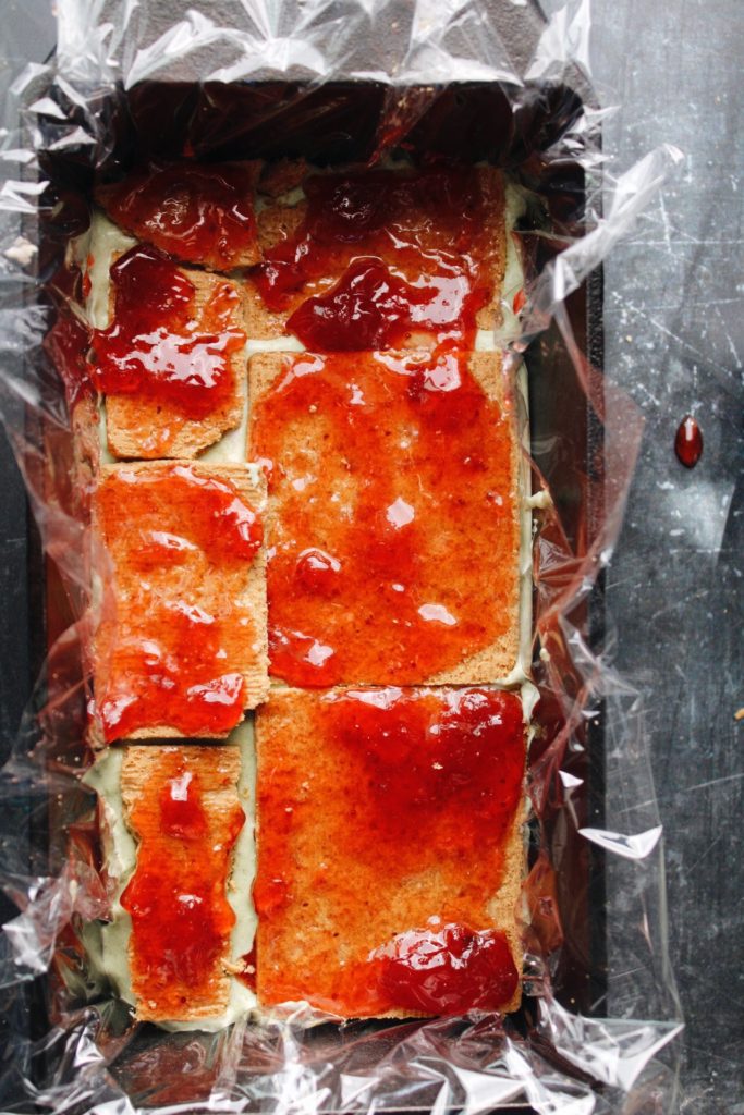 layering of matcha cheesecake with graham crackers and strawberry jam 