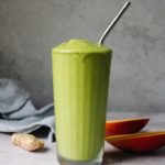 oat milk tropical green smoothie in a clear glass with a metal straw