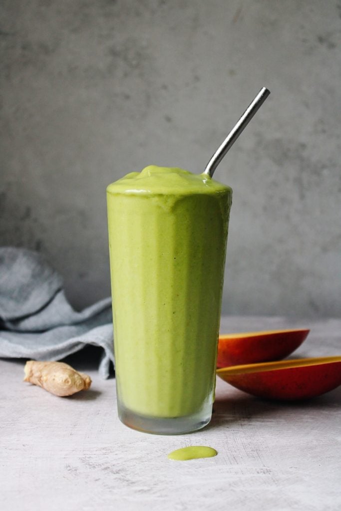 oat milk tropical green smoothie in a clear glass with a metal straw