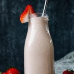 peanut butter and jelly oat milk smoothie in a clear glass milk bottle with a metal straw