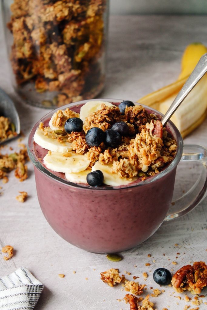cherry berry oat milk smoothie in a large clear glass mug topped with granola and fruit