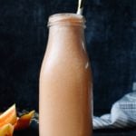 orange peach oat milk smoothie in a glass milk bottle