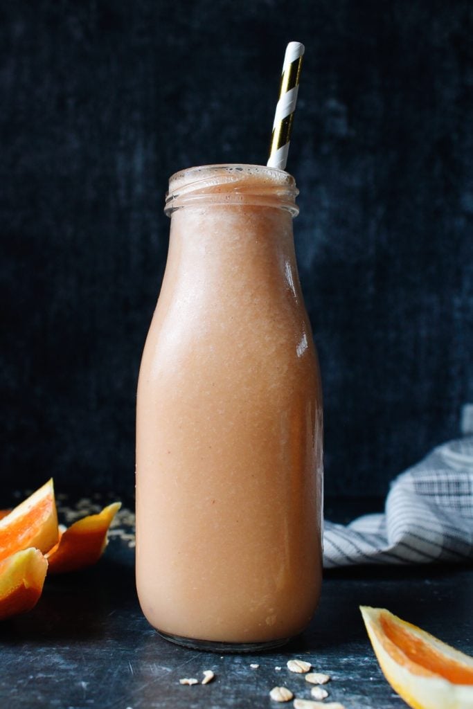 orange peach oat milk smoothie in a glass milk bottle