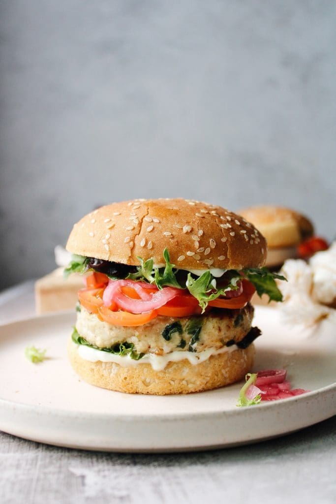 spinach and feta turkey burger on a cream colored plate with lettuce, tomato and pickled onion