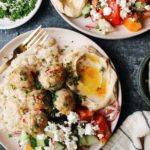 greek chicken meatballs on a plate with rice, hummus, and cucumber tomato salad