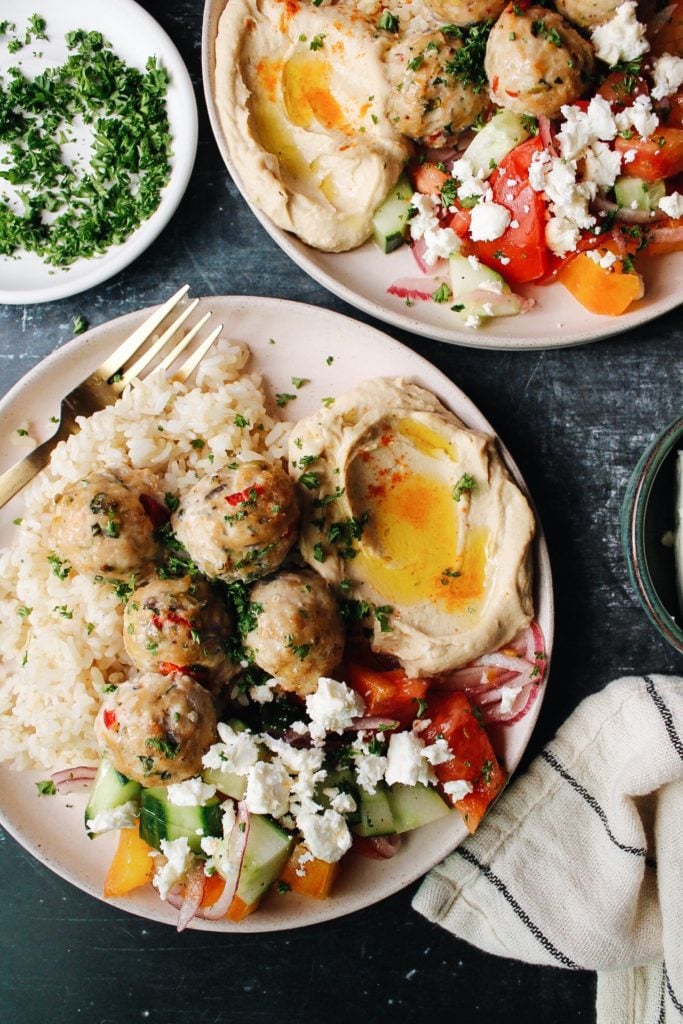 greek chicken meatballs on a plate with rice, hummus, and cucumber tomato salad