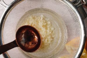 minced garlic lemon juice being pressed through a sieve