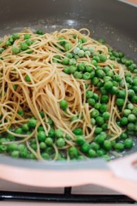pasta and peas added to a pan with garlic butter and sauteed onions