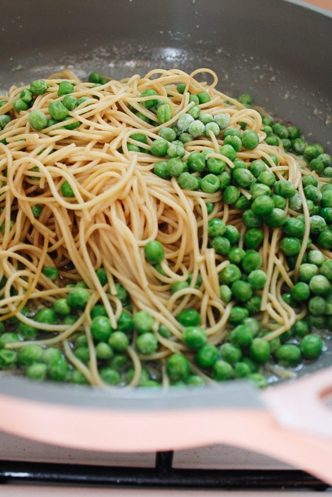 peas and noodles added to a pan with garlic butter and sauteed onions