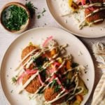 trader joes falafel on plates with rice, veggies, tahini lemon garlic sauce and pickled onions