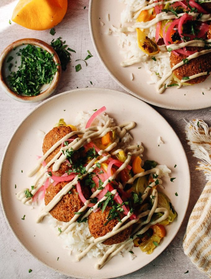 trader joes falafel on plates with rice, veggies, tahini lemon garlic sauce and pickled onions