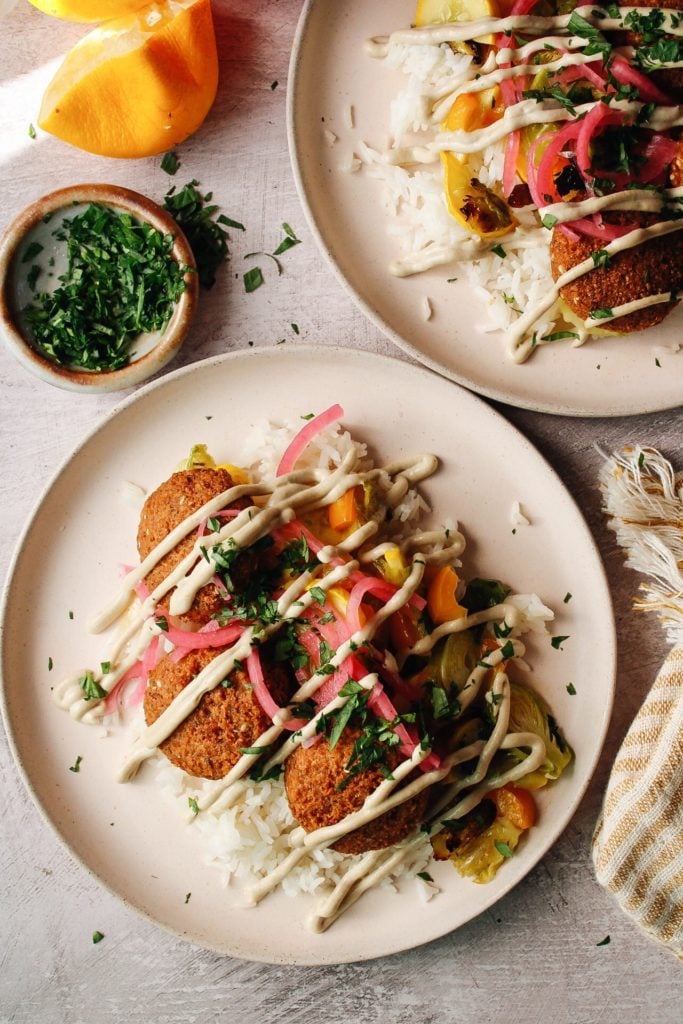 trader joes falafel on plates with rice, veggies, tahini lemon garlic sauce and pickled onions