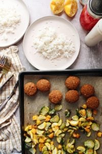 two plates with rice, falafel and roasted veggies are on a baking sheet