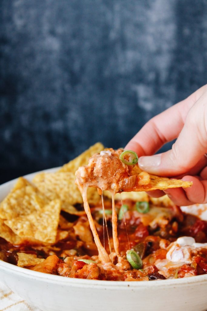 tortilla chip being dipped and pulled out of a bowl of chicken chili, cheese pull is on point