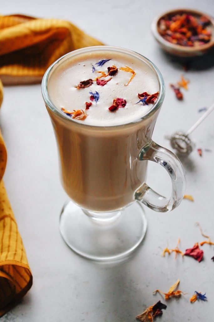 earl grey tea with milk in a clear glass topped with edible flowers