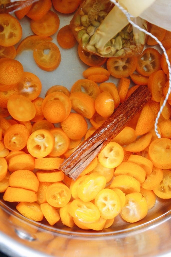 sliced kumquats in water with kumquats seeds and a cinnamon stick