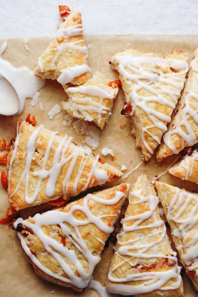 roasted kumquat scones on a baking sheet with a spoon of icing