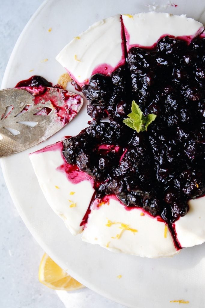 no bake cheesecake with blueberry topping on a white cake stand topped with mint