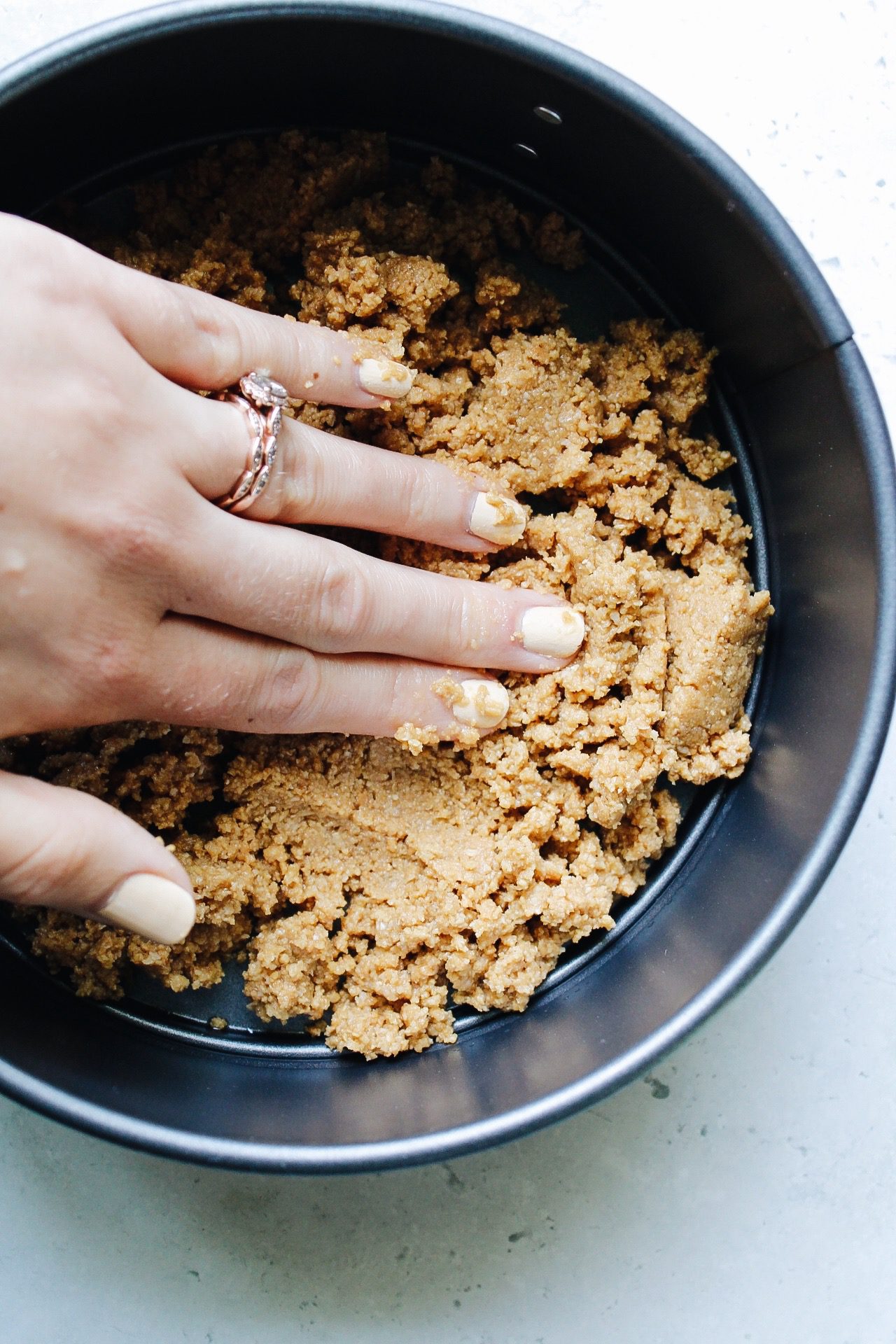 graham cracker crust being pressed into a springform pan