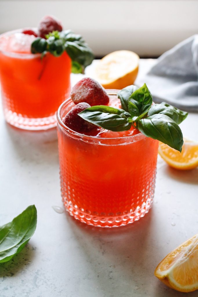strawberry basil lemonade in two clear glasses topped with basil and frozen strawberries