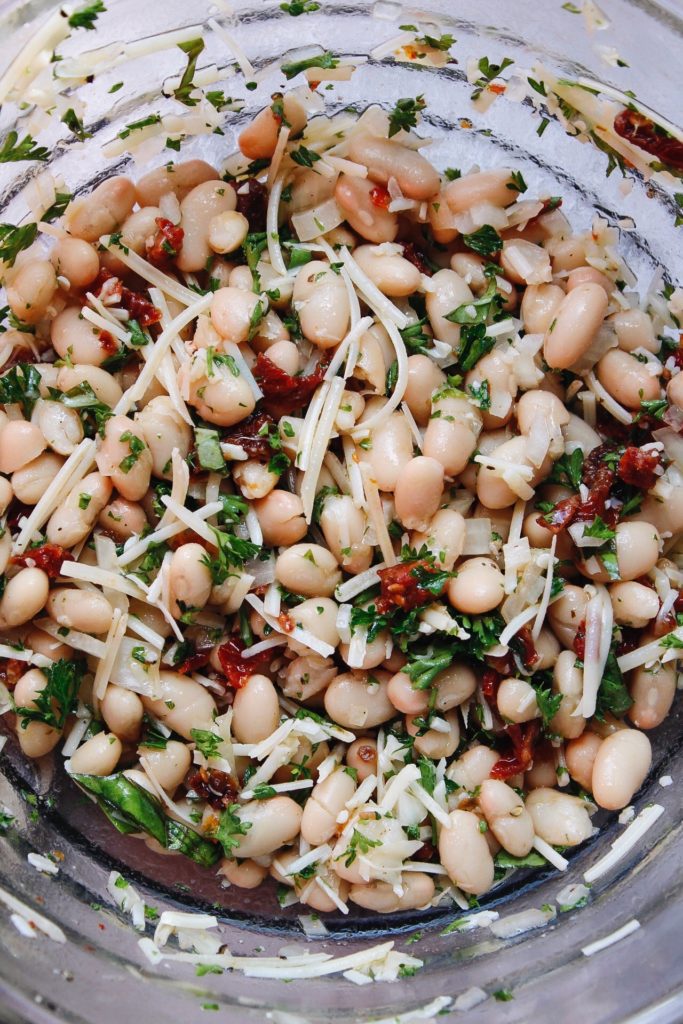 white bean salad in a clear bowl being mixed up