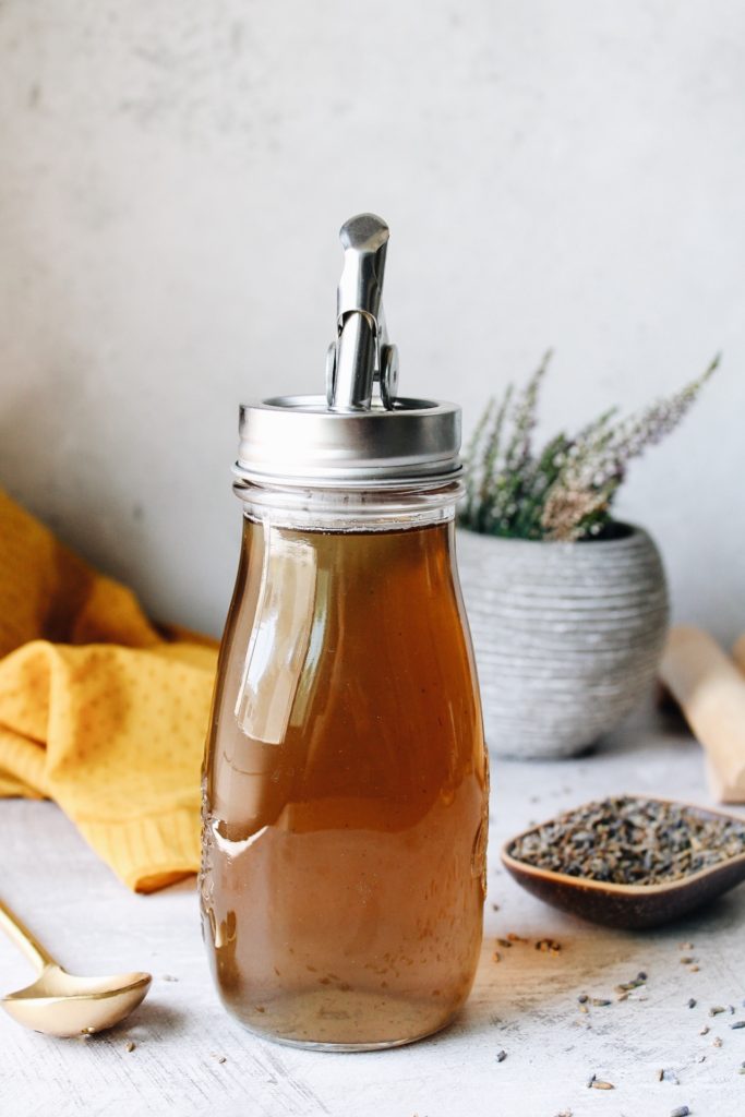 lavender simple syrup in a glass jar with a pour spout