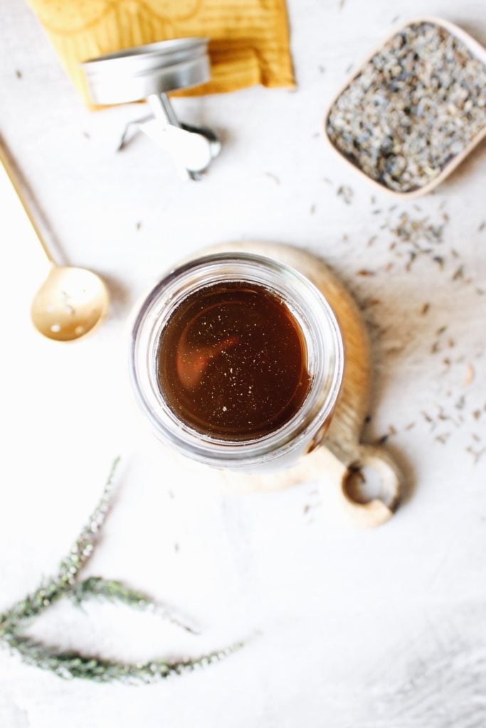 lavender syrup in a glass jar with lavender flowers scattered around it