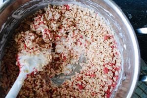 rice krispie cereal being mixed into melted marshmallow mixture with a rubber spatula