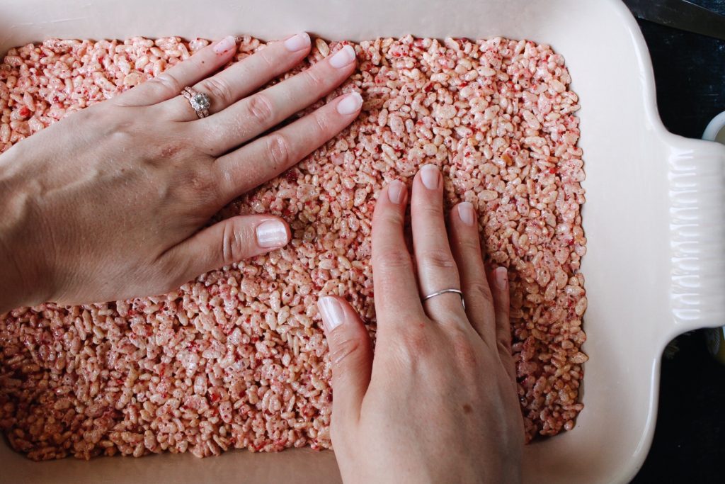 rice krispie treat mixture being pressed into a baking dish with greased hands