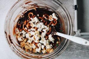 mixing bowl with melted chocolate and fudge mix ins like popcorn, pretzels and peanuts
