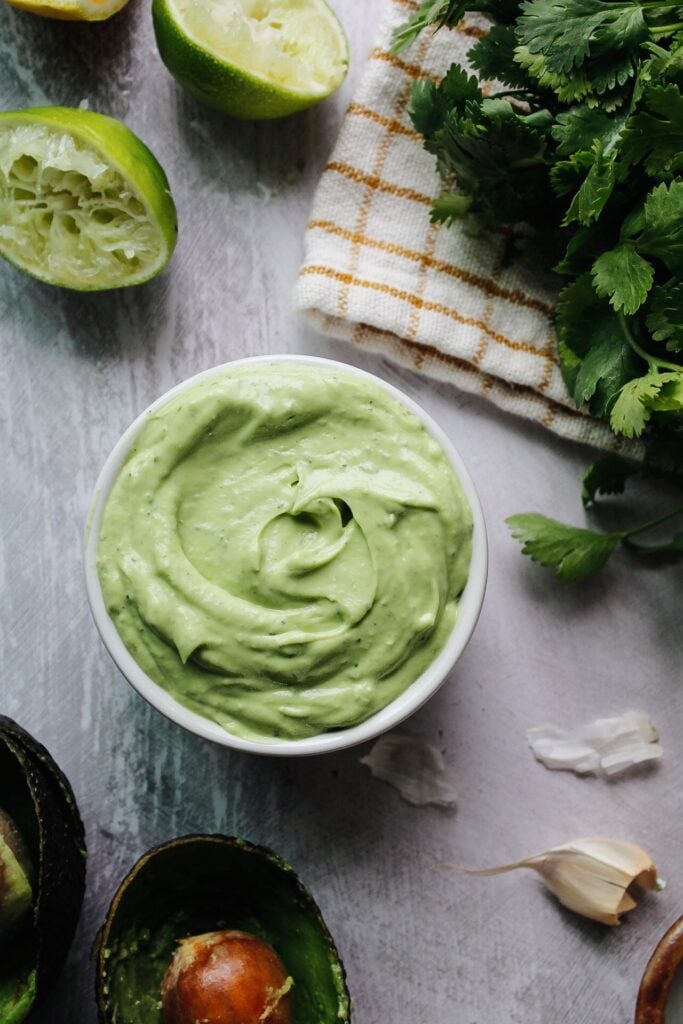 avocado cream sauce in a small white bowl surrounded by ingredients