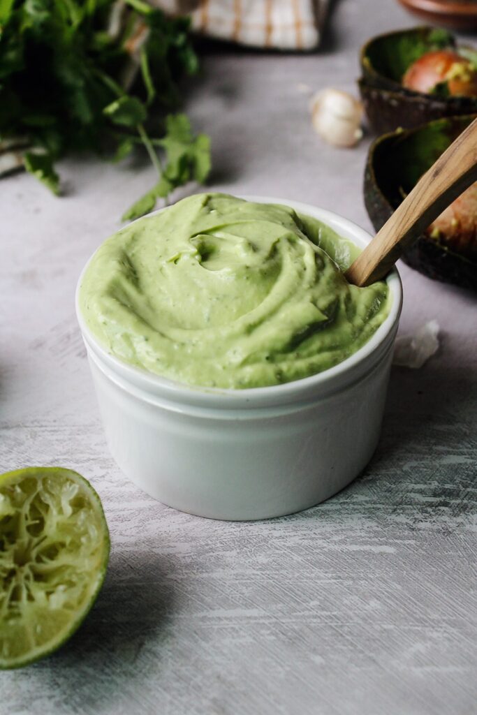 avocado cream sauce in a small white bowl with a wooden spoon
