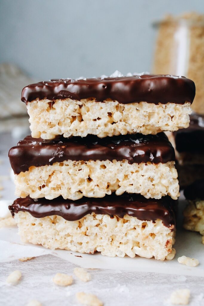 sideview chocolate covered rice krispie treats stacked on parchment paper