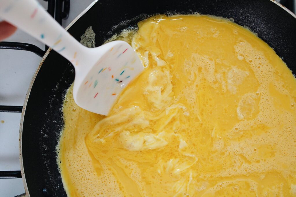 scrambled eggs being cooked in a non-stick skillet with butter